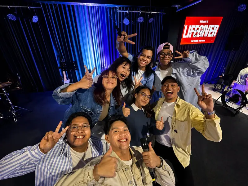 Young people smiling and posing for a group selfie beside the Lifegiver sign